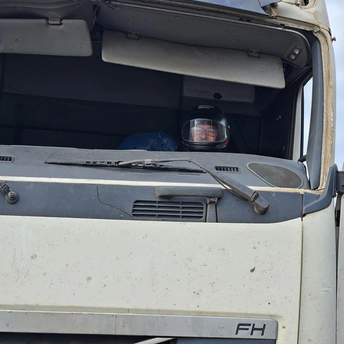 Carreta sem para-brisa, caminhoneiro de capacete, peças amarradas com cordas
